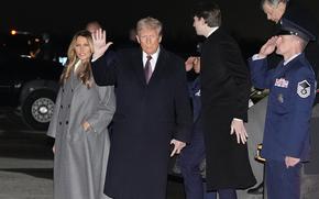 Donald Trump, being saluted by airmen, waves as he walks outside next to his wife.