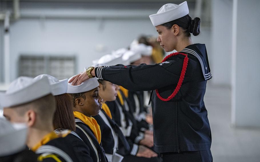 One sailor adjusts another sailor’s cover.