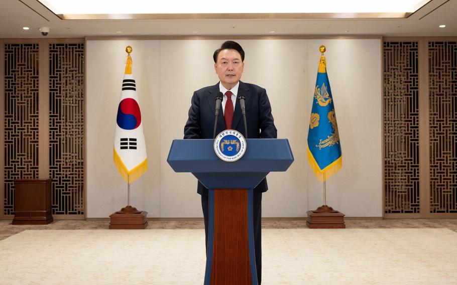 The president of South Korea stands at a podium in an empty room with two flags behind him.