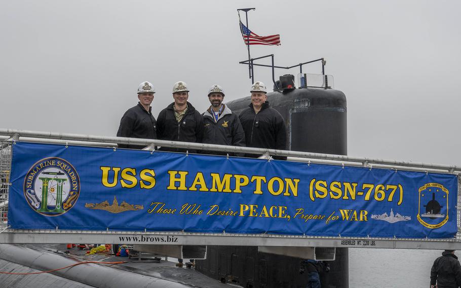 USS Hampton crew poses for a group photo with a banner.