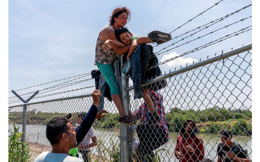 Migrants climb over a barbed wire fence after crossing the Rio Grande into US from Mexico, in Eagle Pass, Texas on Aug. 25, 2023. 