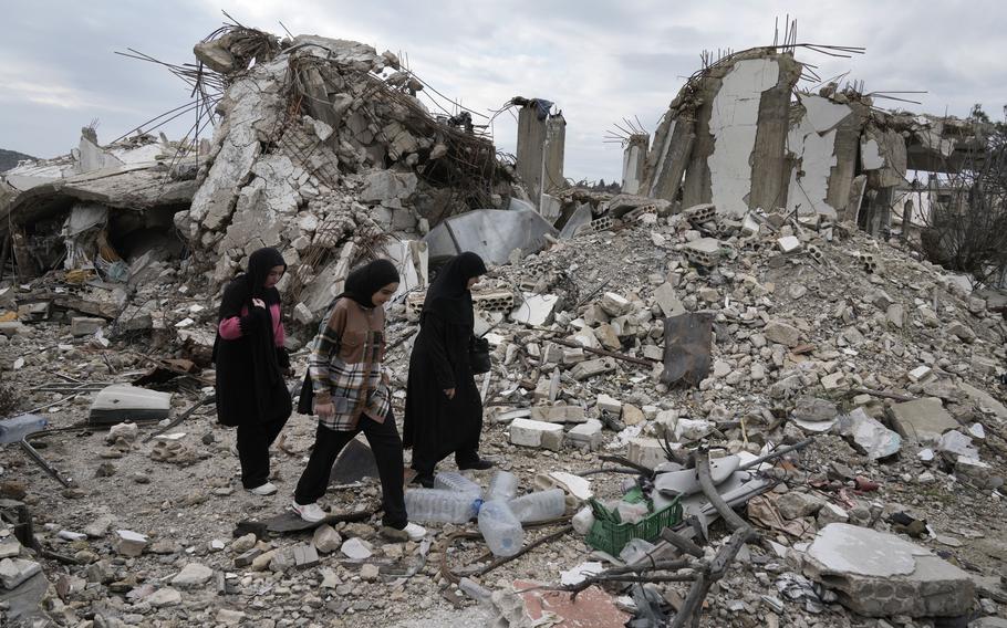 People in Lebanon walk past a destroyed house.