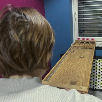 A woman slides a small wooden disc while playing a shuffleboard style game.