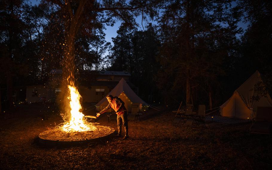 A man tends a campfire near some tents. 