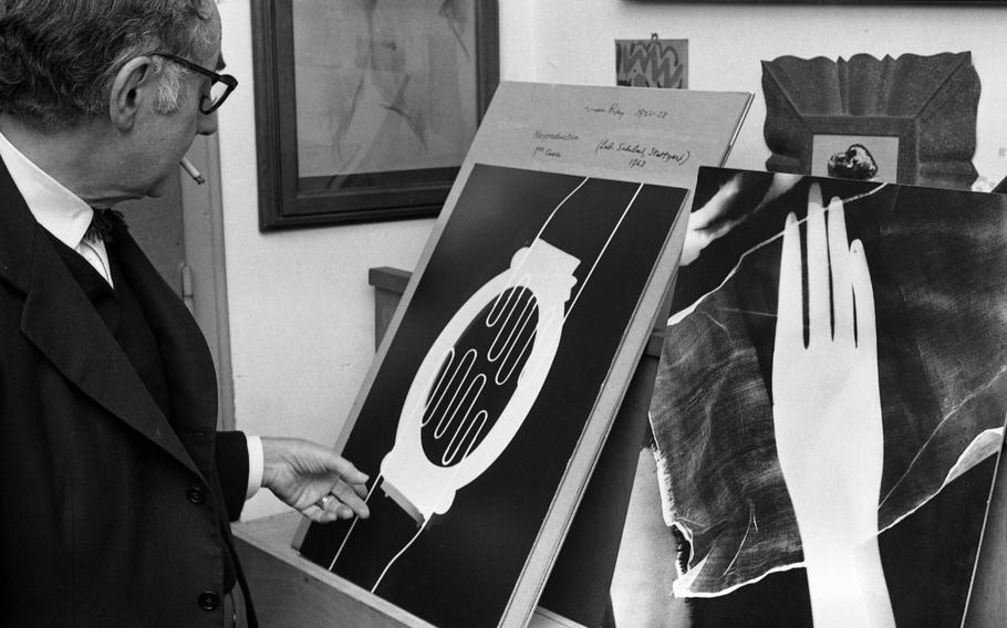 Man Ray stands next to some of his so-called "Rayographs." He made his "rayographs" without a camera by placing objects  - such as hands, coil of wire, and other circular forms - directly on a sheet of photosensitized paper and exposing it to light. The Metropolitan Museum of Art in New York who owns several of the photographic works writes that although the artist had photographed everyday objects before, "these unique, visionary images immediately put the photographer on par with the avant-garde painters of the day. Hovering between the abstract and the representational, the rayographs revealed a new way of seeing that delighted the Dadaist poets who championed his work, and that pointed the way to the dreamlike visions of the Surrealist writers and painters who followed."