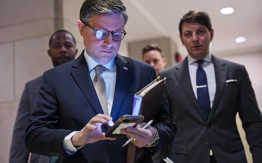 House Speaker Mike Johnson looks down at his phone while a folder is tucked between his body and arm.