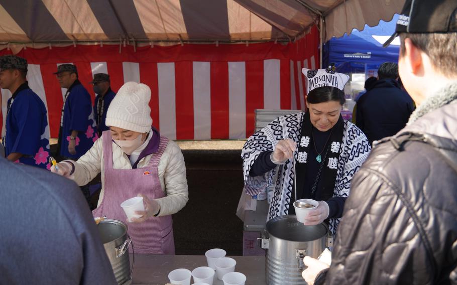 Two women hold ladles and cups as people wait in front of them in line. 