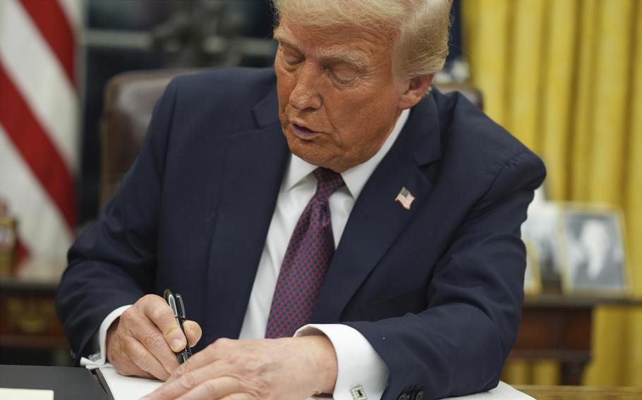 Donald Trump signs an executive order at his desk.