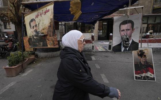 A woman walks outside past hung pictures of the ousted Syrian president with shoes beside them.