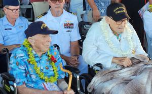 Two elderly men sit side by side in wheelchairs, each wearing a hat that says Pearl Harbor survivor.