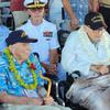 Two elderly men sit side by side in wheelchairs, each wearing a hat that says Pearl Harbor survivor.