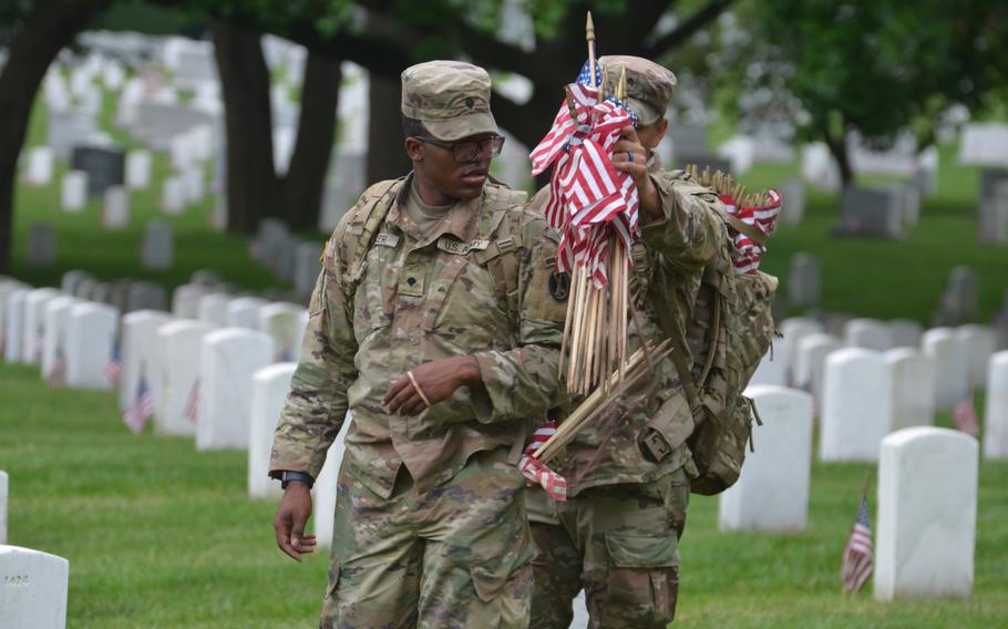 A member of The Old Guard reaches into a soldier’s backpack for more flags to place at graves in Arlington National Cemetery on Thursday, May 23, 2024, to honor the fallen service members for Memorial Day.