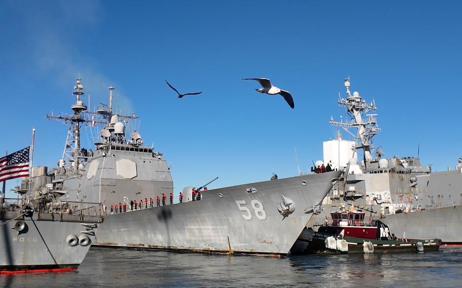 Sailors stand by the rails an seagulls fly overhead.