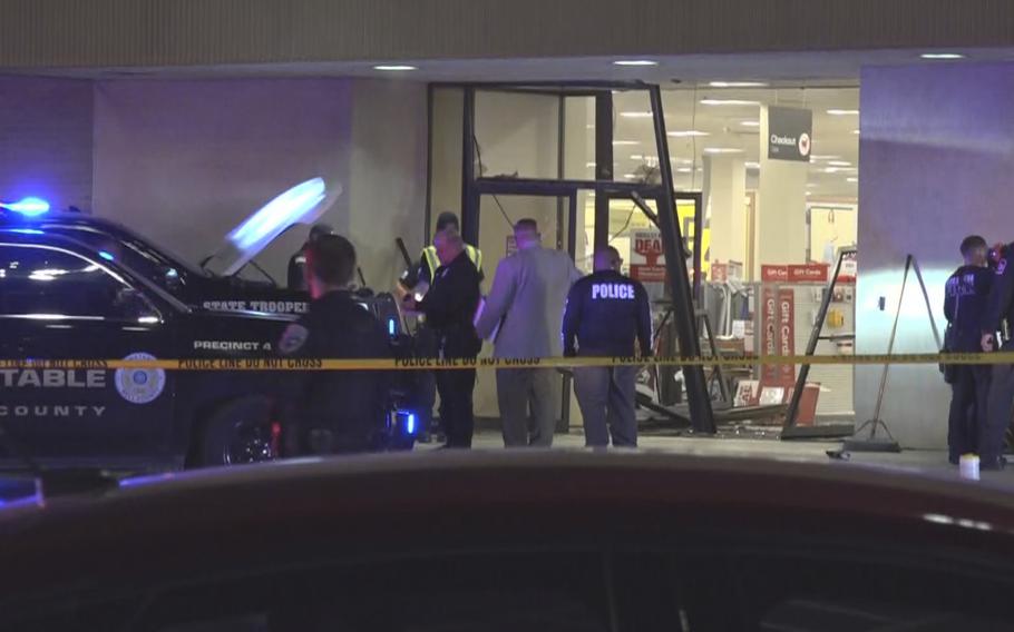 Police officials stand in front of a broken glass door at a shopping mall.