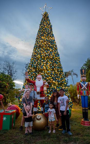 Families pose for a group photo in front of the tree, with a Santa figure behind them.  