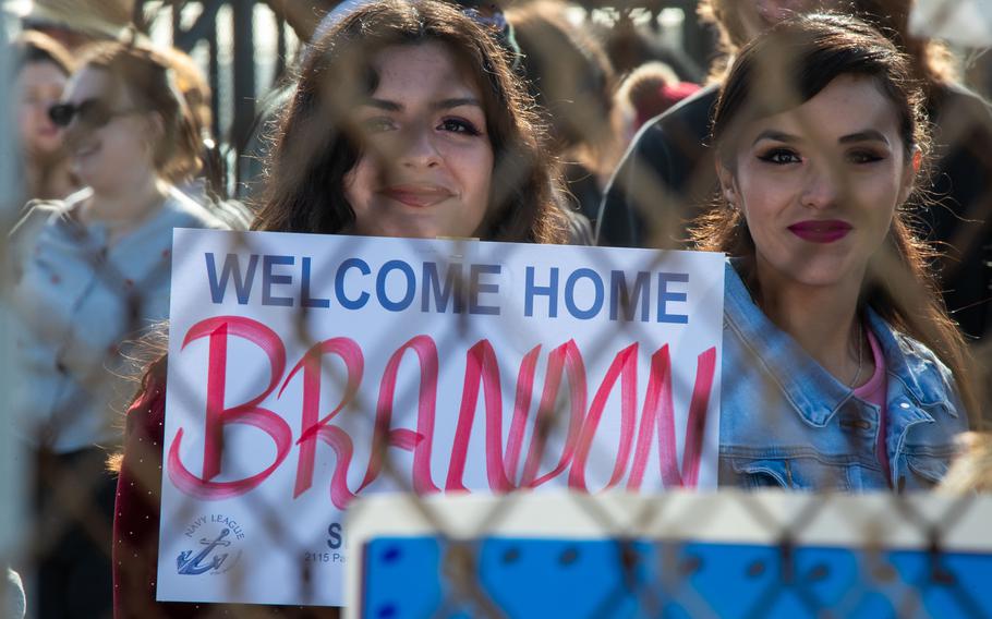 A lady holds a welcome home sign behind a fence