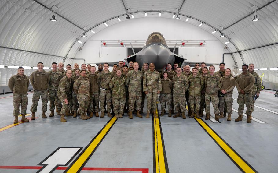 Airmen gather in a hangar with three yellow vertical lines on the floor.