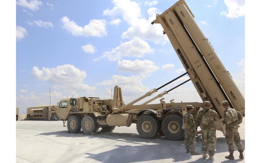 Soldiers stand in front of a missile defense system.