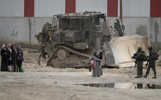 Palestinian women standing in front of soldiers, all of them before a large bulldozer.