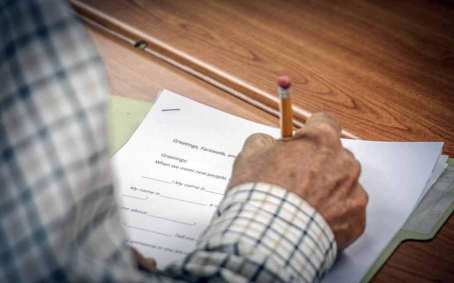 A man grips a pencil as he writes as part of an assignment related to English greetings and farewells.