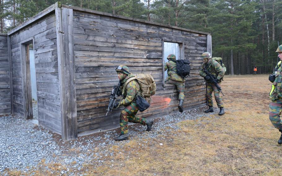 Soldiers running an exercise, taking cover behind a small cabin.