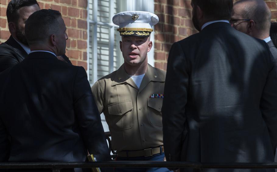 A Marine Corps officer in dress uniform stands outside a courthouse while surrounded by lawyers in suits.