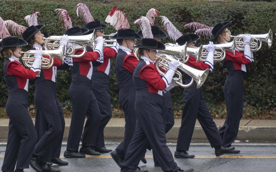 A marching band in uniform marches and plays horns.