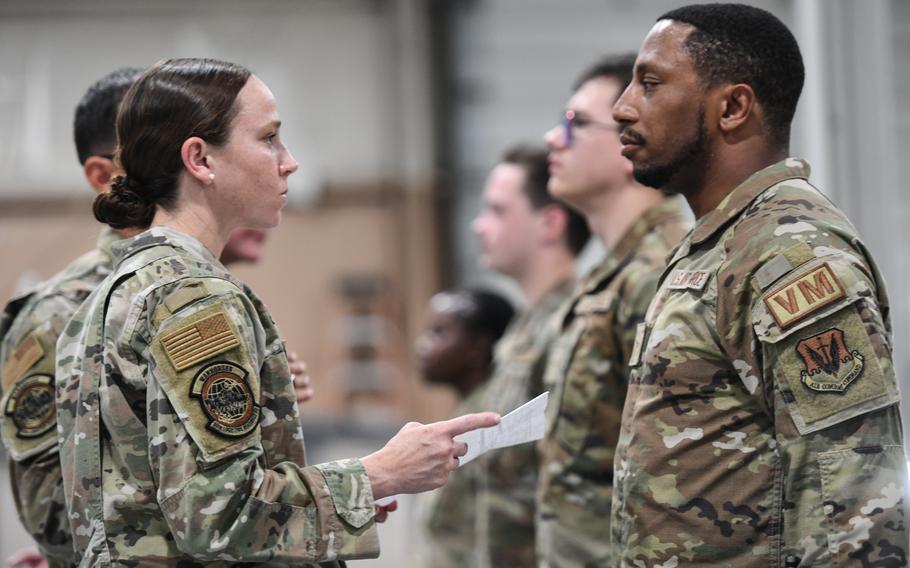 A female airman holds a piece of paper while looking at a bearded male airman. 