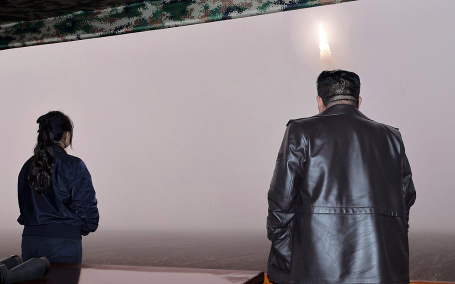 North Korean leader Kim Jong Un in a leather jacket watches a missile launch with his daughter beside him.