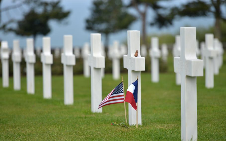 An American flag waves in the breeze beside a French flag before a headstone at Normandy American Cemetery at Colleville-sur-Mer, France. The cemetery is the final resting place for 9,387 American war dead.