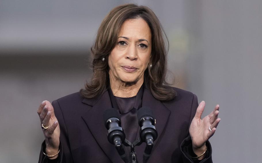 Kamala Harris stands on a stage and speaks into a bank of microphones.