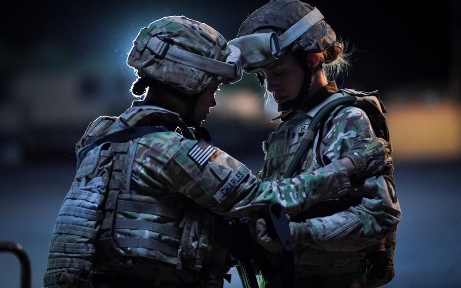 Two women in Army fatigues at night, one grabbing the other’s shoulder.