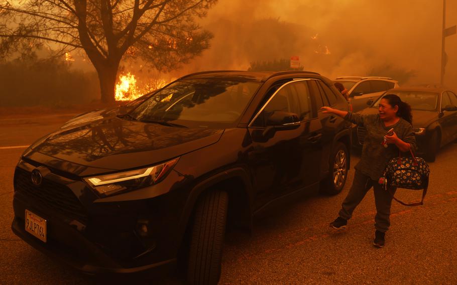 A woman gets into a car as a wildfire burns in the background.