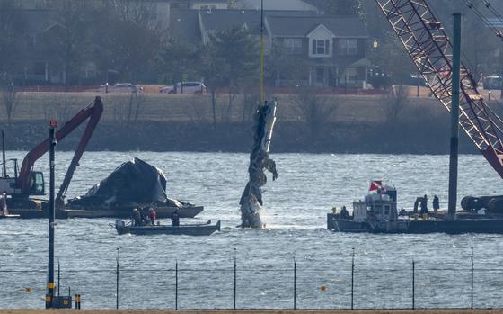 Part of a plane is lifted out of the Potomac River with some houses and cars seen in the backround.