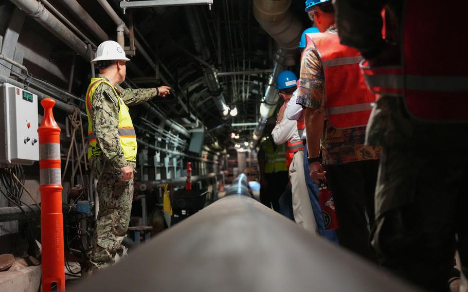 A Navy officer in camouflage uniform, reflective vest and helmet points in a tunnel of an underground fuel storage facility.