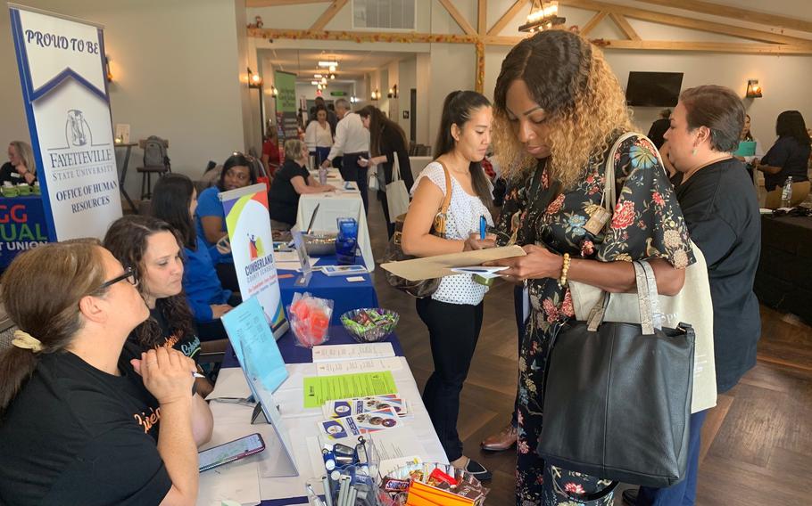 A woman fills out a document at a table staffed with workers during a career expo.