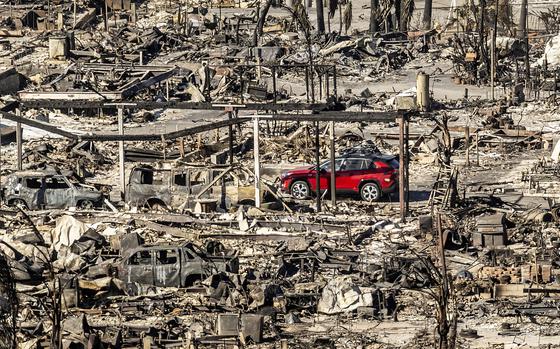 A car drives past homes and vehicles destroyed by the Palisades Fire at the Pacific Palisades Bowl Mobile Estates on Sunday, Jan. 12, 2025, in Los Angeles. (AP Photo/Noah Berger)