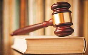 A stock photo of a gavel resting on a book on top of a desk.