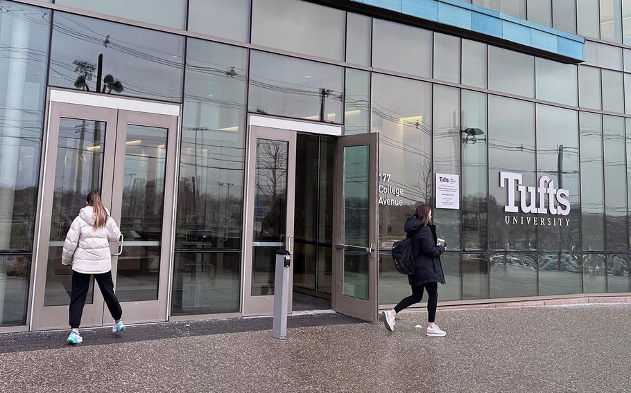 Two people walk in and out of doors by a glass building.