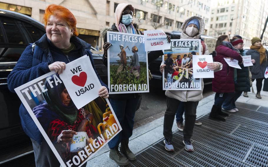 Protesters hold signs that say We love USAID and the faces of foreign aid, with photos of people.