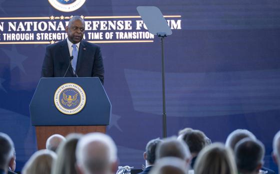 The defense secretary wearing a suit speaks to an audience from a podium on a stage.