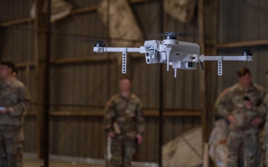 A drone flies with three soldiers in the background.