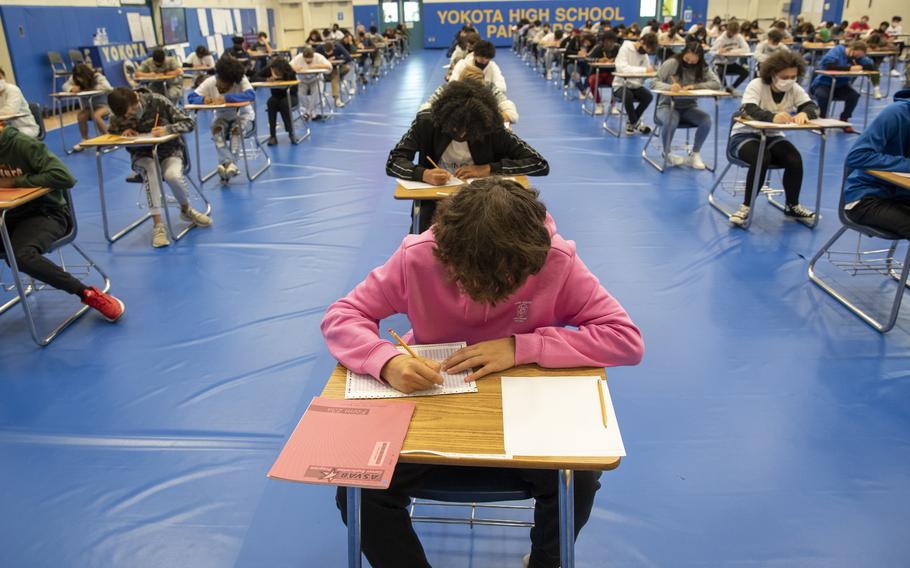 Young people sitting at desks in rows in a gym.