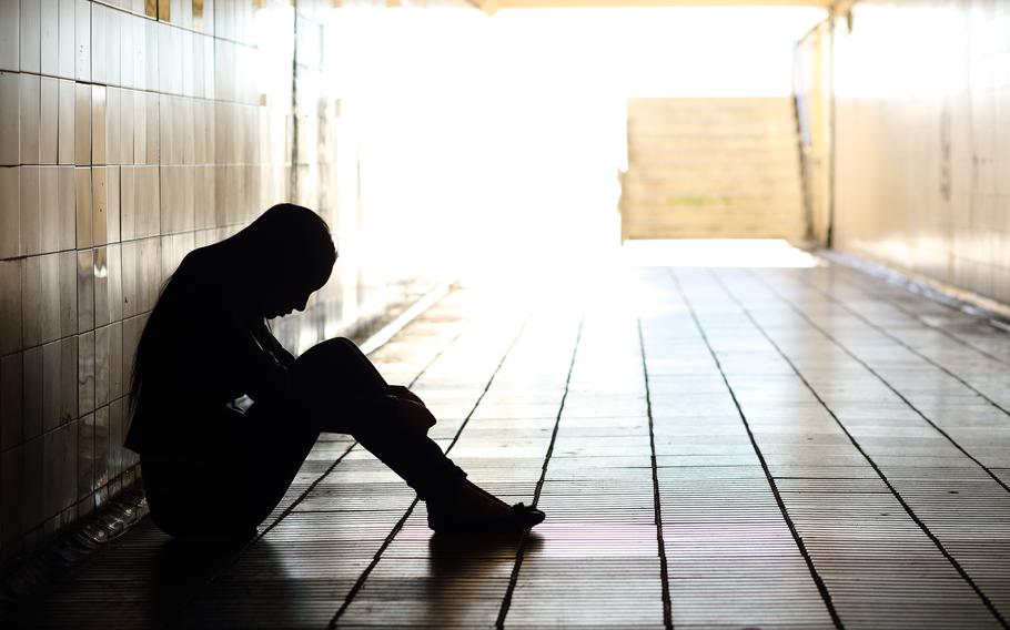 A young person sitting against a wall