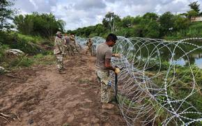 Several troops work on wire barriers along a river bank.