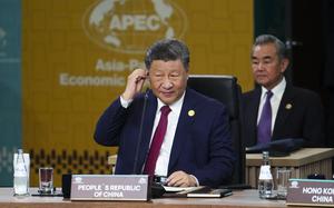 The president of China sits at a desk and adjusts an earpiece.