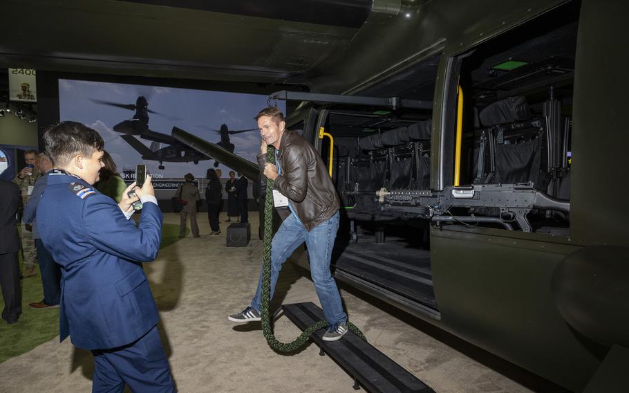 A service member takes a picture of another man posing with an Osprey helicopter.