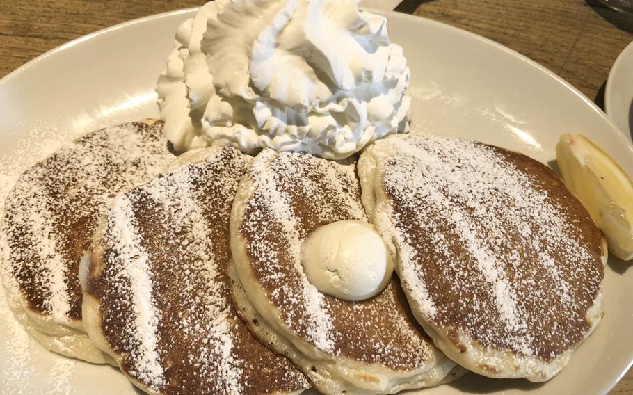 Pancakes with powdered sugar, butter and whipped cream rest on a plate.