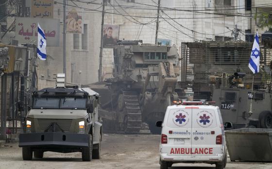 An ambulance and armored truck are seen side-by-side in the foreground while a bulldozer operates behind them.