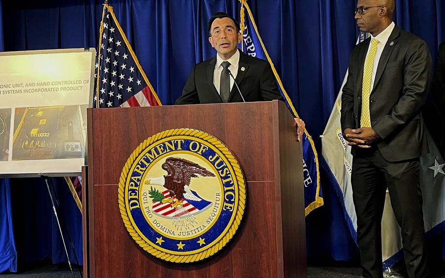 A man in a dark suit stands at a podium with a Department of Justice emblem.